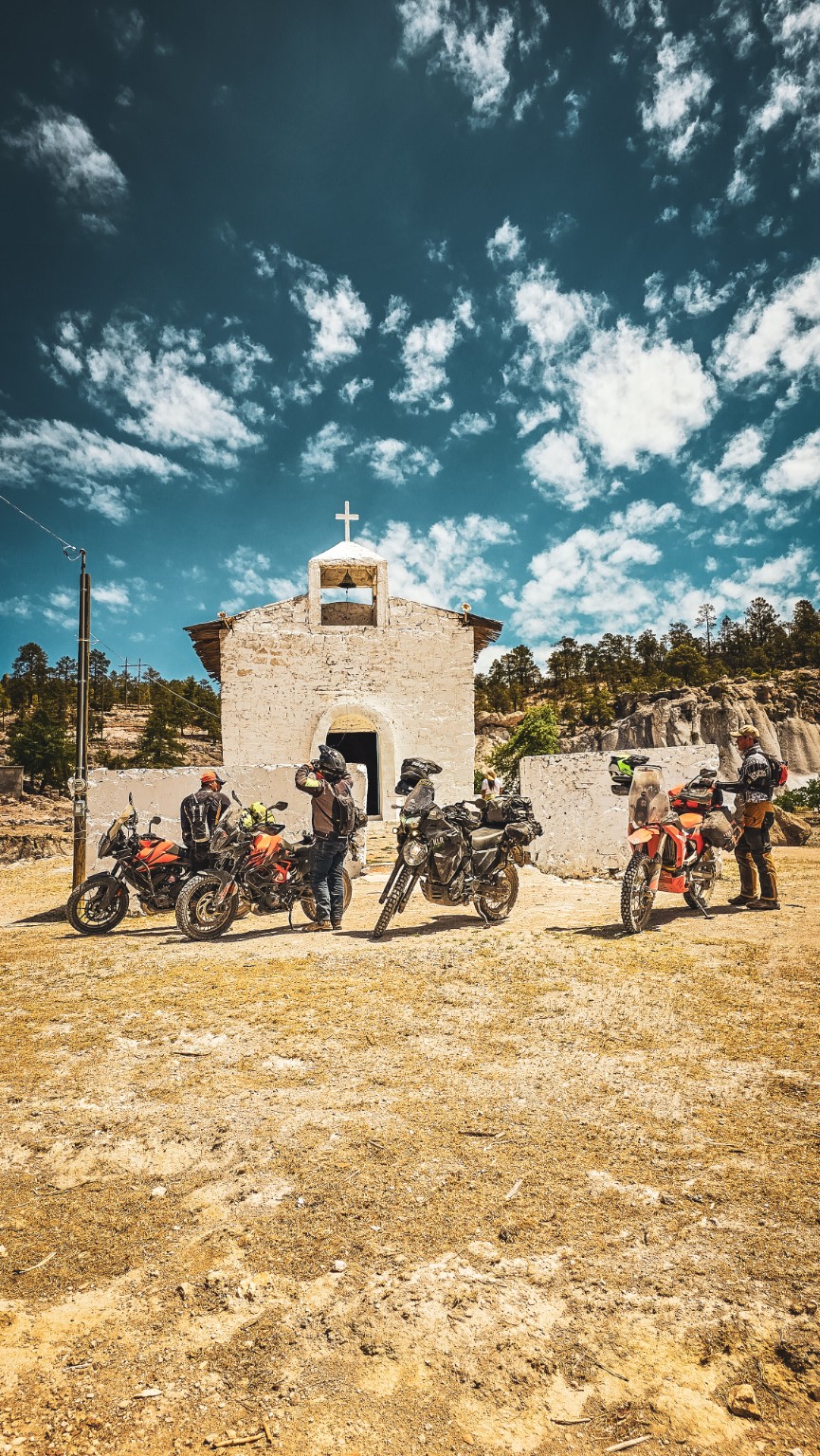 Pilotos con sus motocicletas frente a una pequeña iglesia de piedra