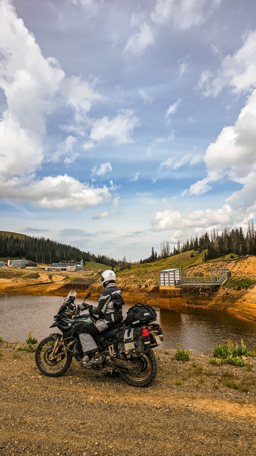 Moto junto a un lago rodeado de montañas y bosque