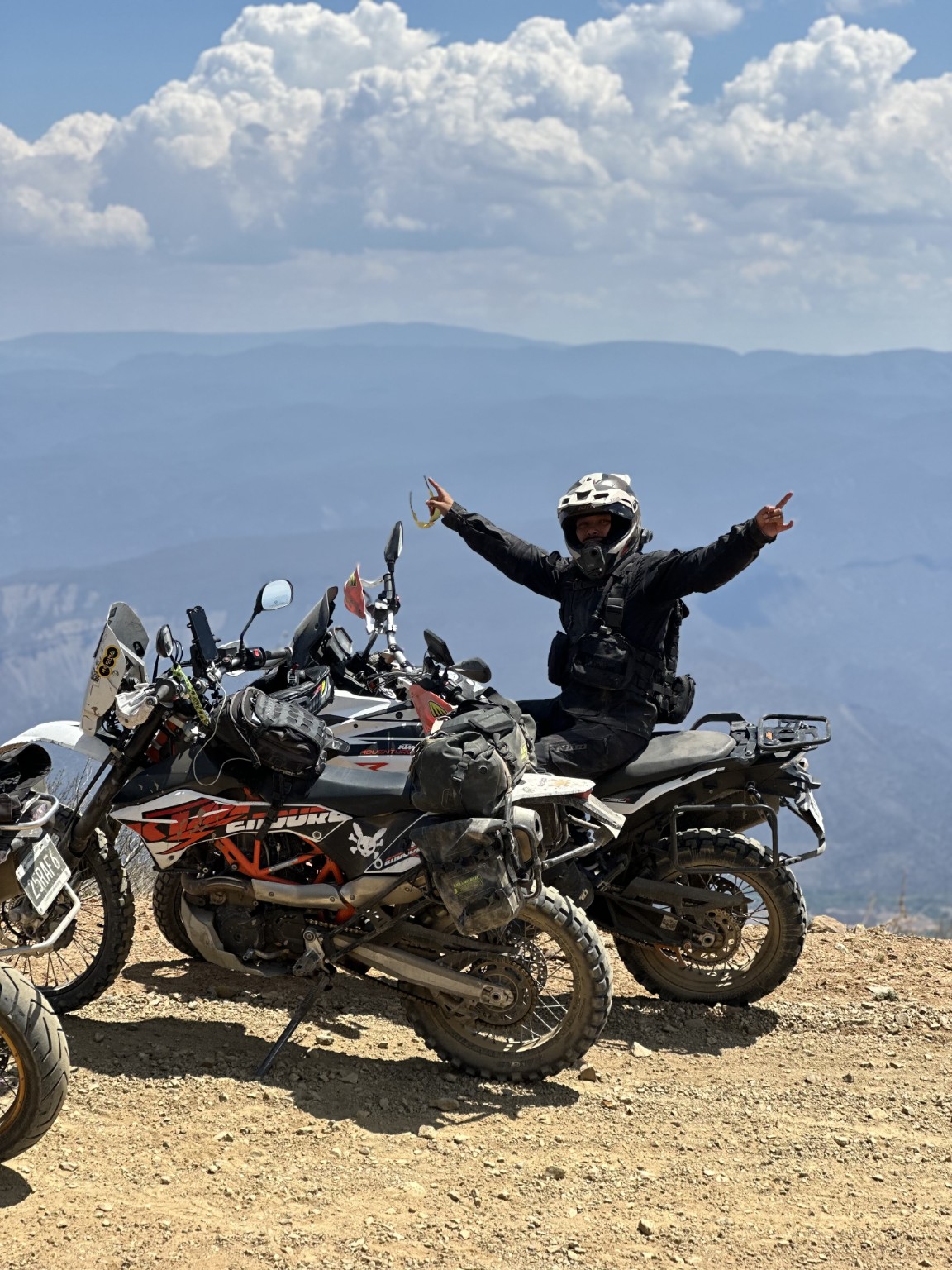 Piloto junto a motocicletas Adventure con vistas a un valle